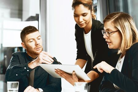 Three professionals collaborating over a digital tablet, emphasizing teamwork, shared insights, and strategic decision-making.