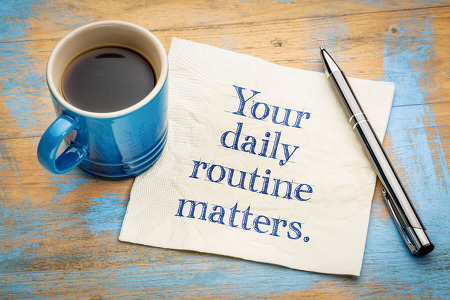 Blue coffee mug with coffee on top of a napkin that says Your daily routine matters