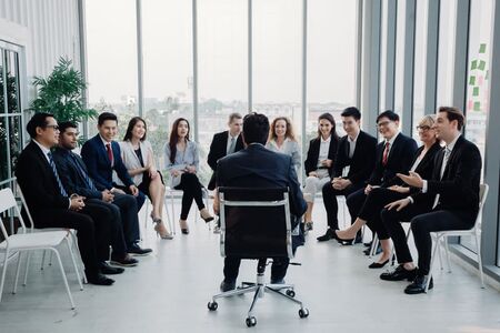 Business team sitting in a circle during corporate training session led by a facilitator, promoting leadership development, teamwork, and communication skills in a modern office setting.