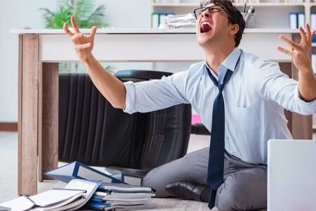 Frustrated businessman sitting on the office floor with papers scattered, showing stress, burnout, and workplace overwhelm.