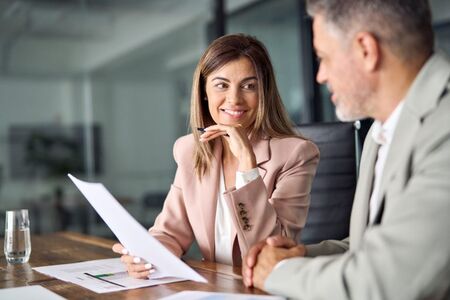 Businesswoman in a pink blazer smiling during a coaching session, engaged in discussion with a colleague, representing executive coaching and leadership development.