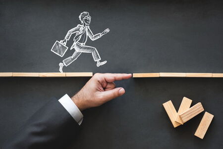Concept of business support and leadership coaching shown by a hand bridging a gap with wooden blocks, helping a chalk-drawn businessman with a briefcase run across.