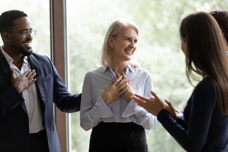 Diverse business team applauding senior female leader in office, showing workplace appreciation, recognition, and employee engagement.