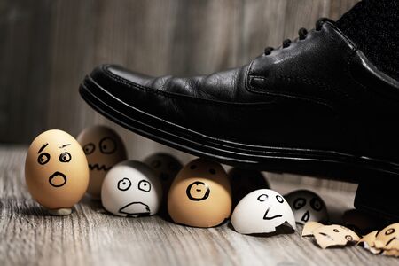 Black leather shoe stepping on eggs with drawn emotional faces, symbolizing workplace stress, fear, and pressure
