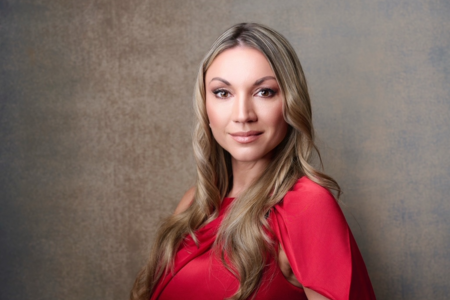 Professional headshot of a Anna Barnhill in a red dress posing against a neutral studio backdrop, symbolizing leadership, confidence, and executive presence.