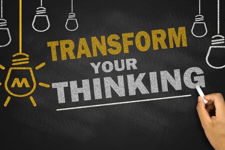 Transform your thinking concept on chalkboard with hand writing motivational phrase and light bulb icons symbolizing creativity and mindset shift.