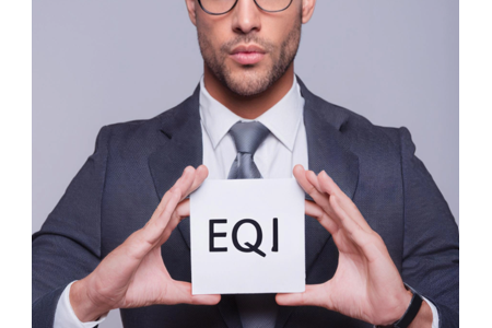 Confident businessman in a suit and glasses holding a white cube with the letters ‘EQI,’ representing emotional intelligence quotient.