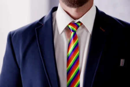 Close-up of a businessman in a navy suit and white shirt wearing a rainbow-striped lgbtqia tie.